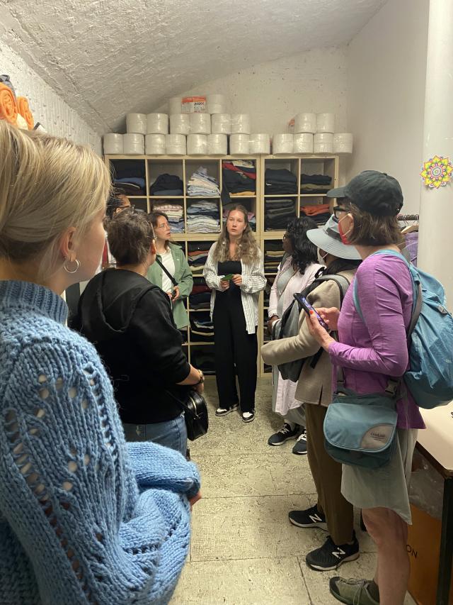 People stand in a room listening to a woman talk