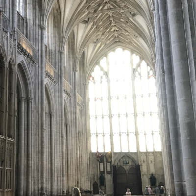 Winchester Cathedral, interior view, grey stone columns, looking towards a large clear stained glass window at the rear of the cathedral.