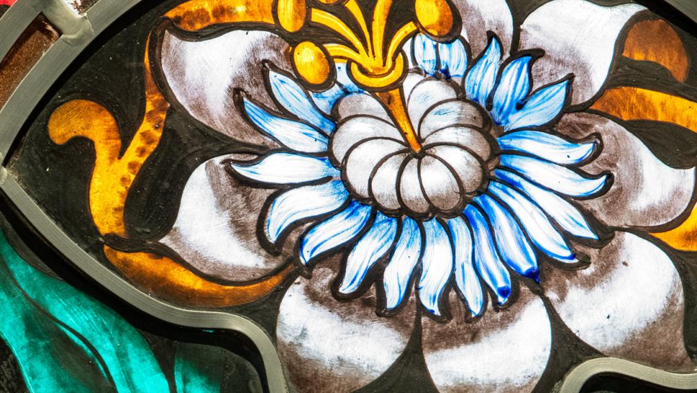 Stained glass image of a large white flower surrounded by green leaves