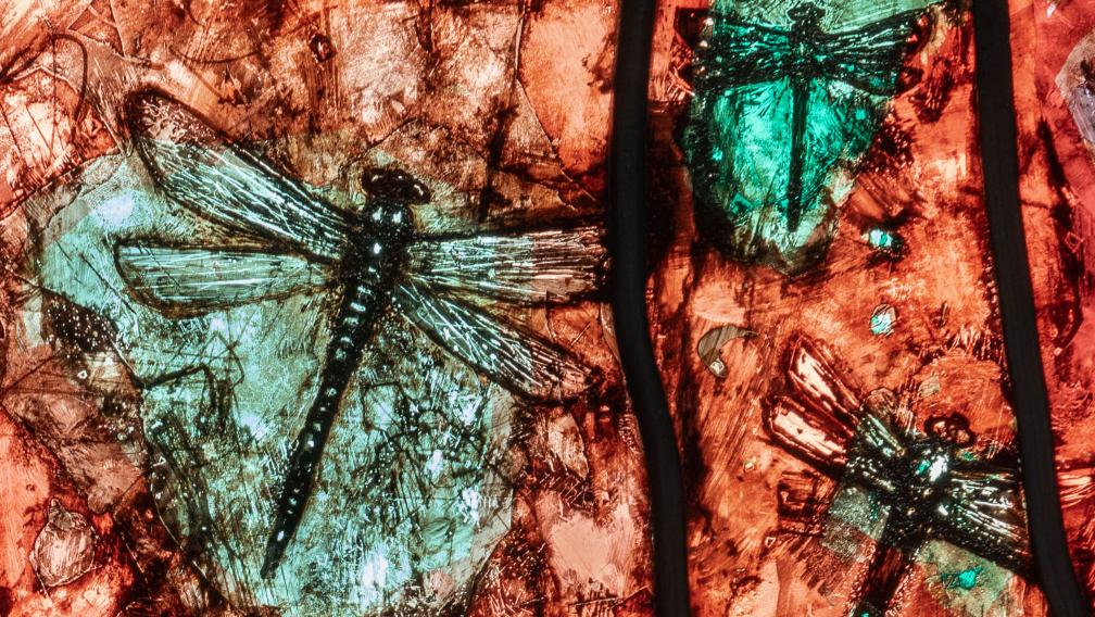 Turquoise dragonflies against a red backdrop, depicted in stained glass