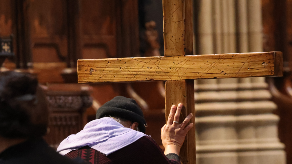 A person bends before and places their hand on a wooden cross in Trinity Church