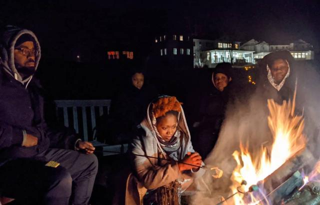 A group of adults, bundled up in coats and hoods, roasts s'mores