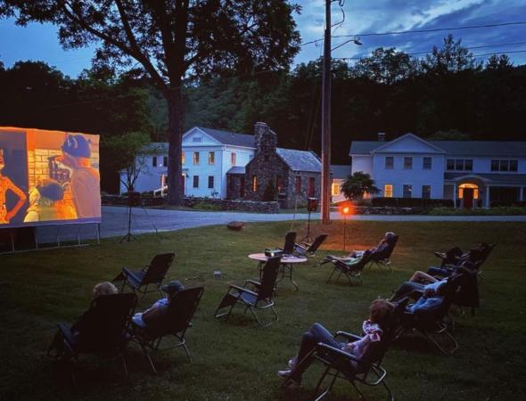 Socially-distant movie night. Film projected onto a screen and chairs arranged in the grass as night falls