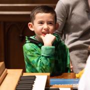 A child smiles as they perch on the edge of a keyboard in Trinity Church