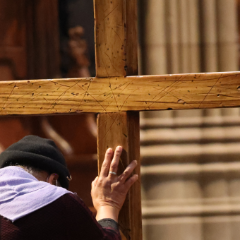 A person bends before and places their hand on a wooden cross in Trinity Church